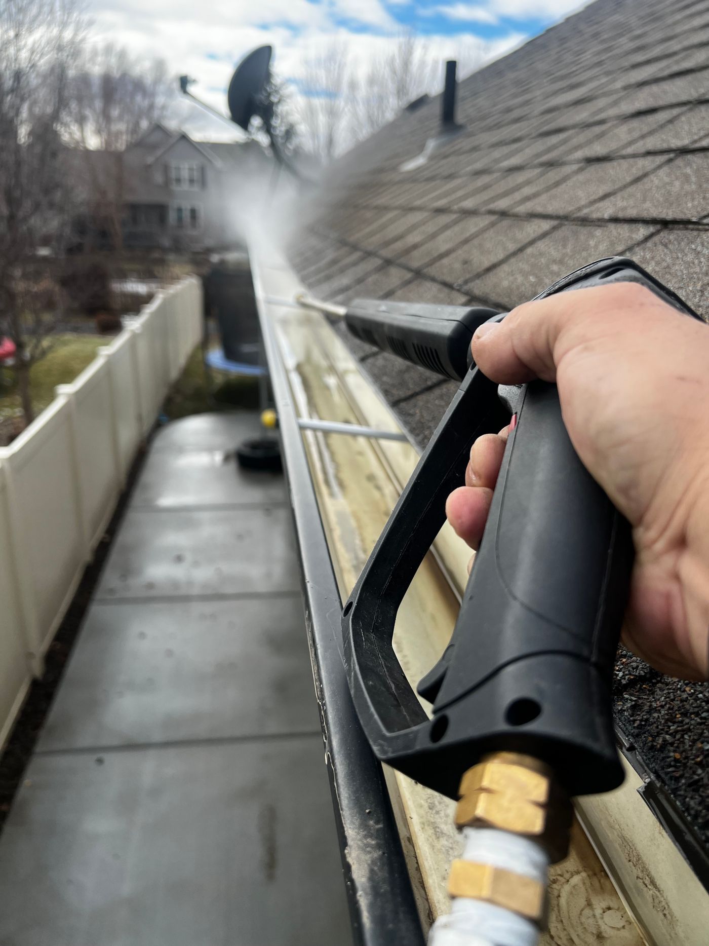 Close-up of a gutter being rinsed beside a shingled roof